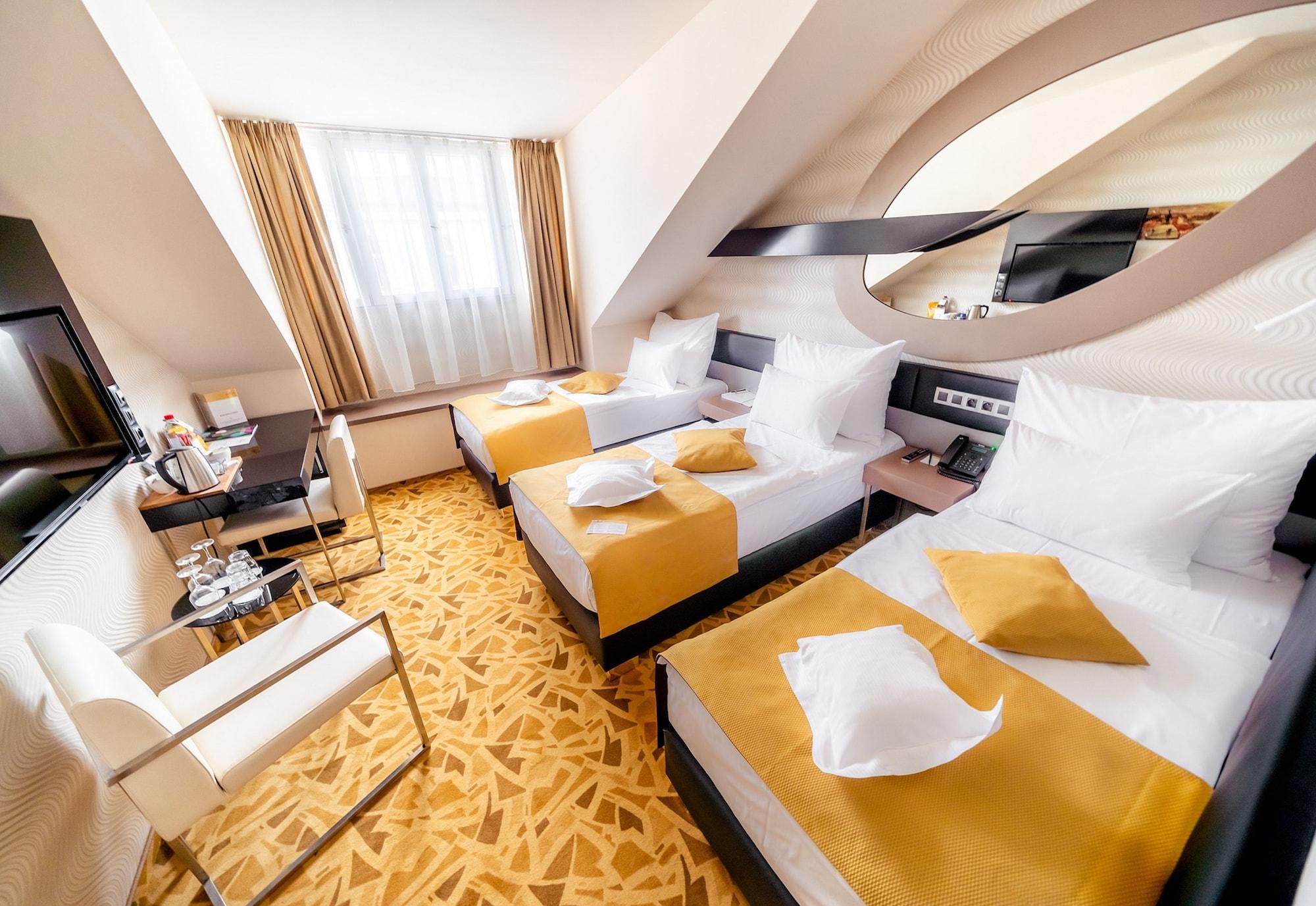 Grandium Hotel Prague Exterior photo The photo shows a hotel room featuring two twin beds, each made up with white linens and yellow decorative pillows. The room has a modern design with a light color scheme, including soft yellow tones. There's a large window letting in natural light, 
