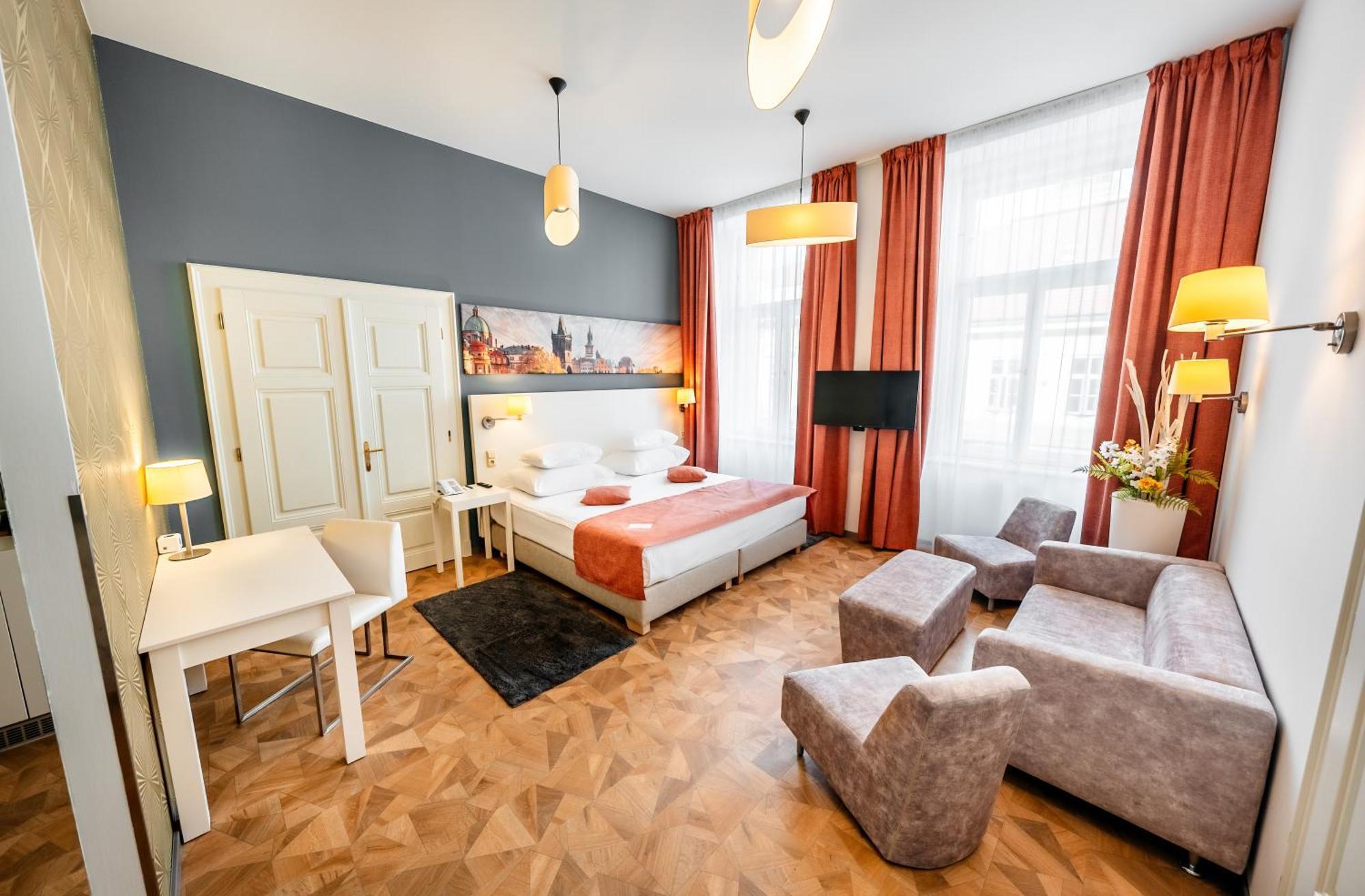 Grandium Hotel Prague Exterior photo The photo shows a stylish hotel room with a contemporary design. It features a double bed with a white and orange color scheme, accompanied by bedside lamps. There is a large window with sheer curtains that allows natural light to brighten the space.