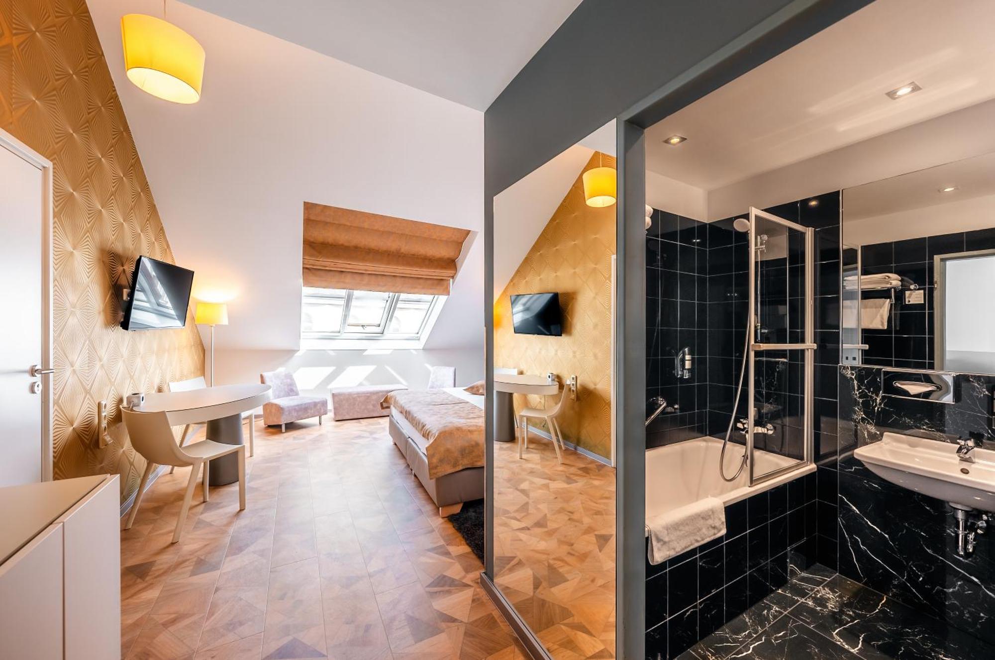 Grandium Hotel Prague Exterior photo The photo shows an interior of a hotel room featuring a modern design. On one side, there are two beds with white linens, a desk, and a television mounted on the wall. The room has sloped ceilings and large windows that let in natural light. 

Adjace