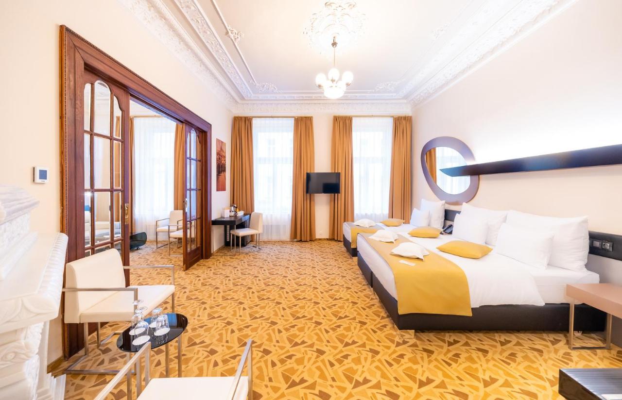 Grandium Hotel Prague Exterior photo The photo shows a spacious hotel room with an elegant design. There are two large beds with white bedding, accented with yellow pillows. The room has tall windows with flowing curtains that allow natural light to brighten the space. A flat-screen tel